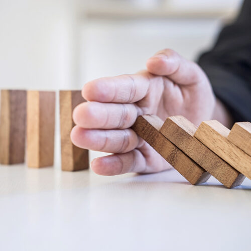 Hand halting a row of wooden blocks as a domino-style stack tips forward
