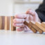 Hand halting a row of wooden blocks as a domino-style stack tips forward